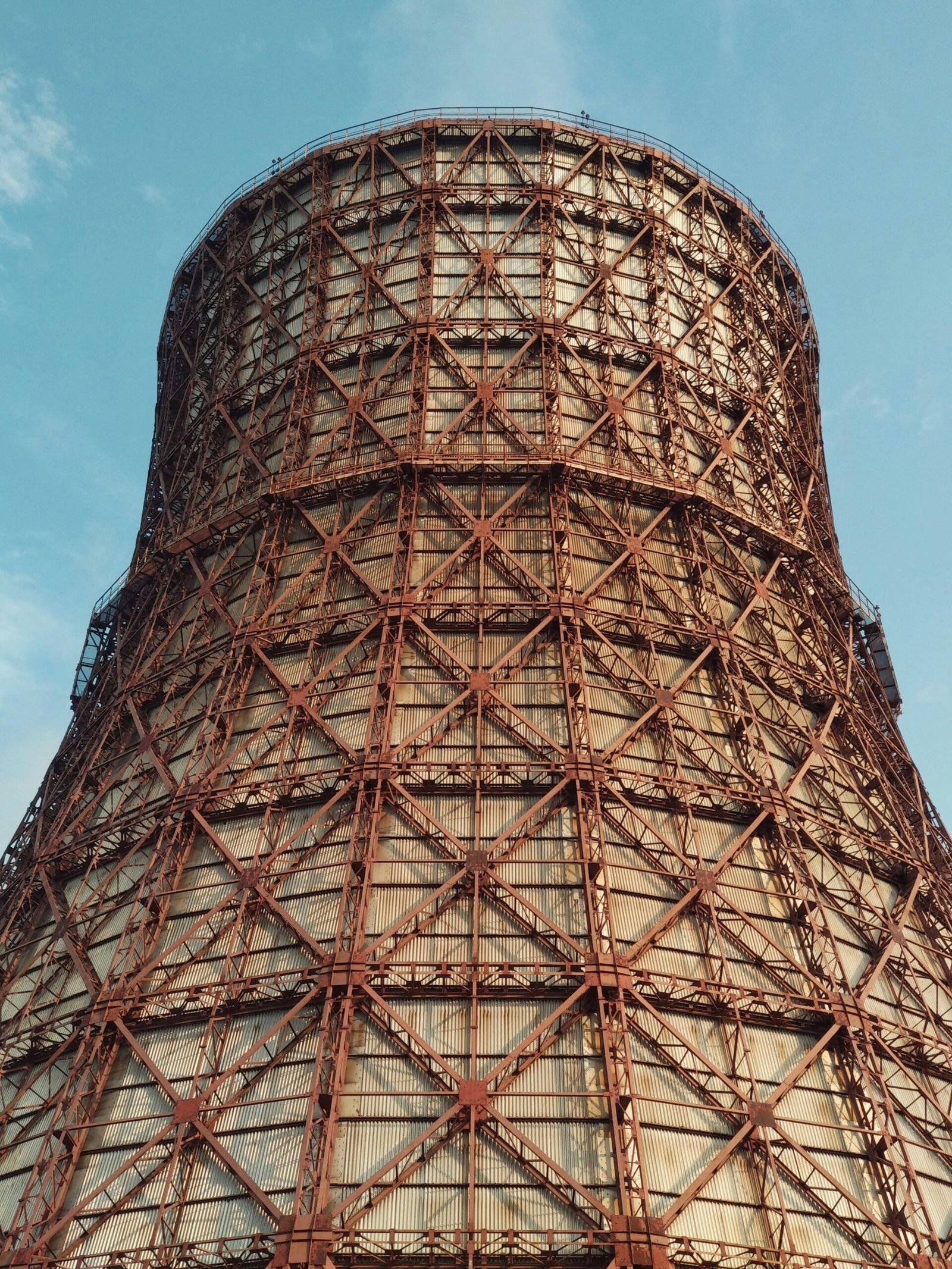 A low angle view of a towering industrial cooling tower against a clear blue sky.