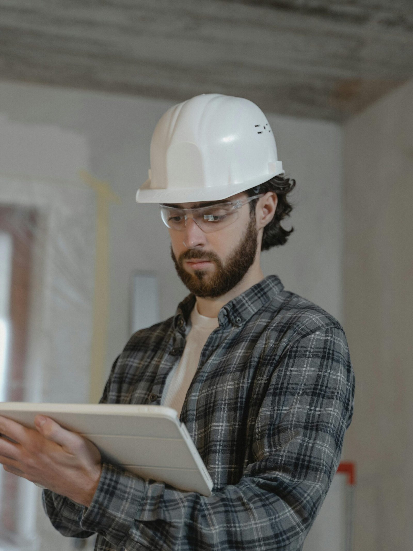 Male construction engineer assessing building plans indoors, wearing a hard hat.